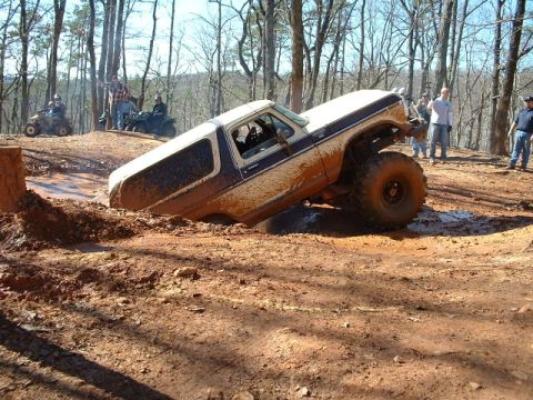 1992 Ford Mustang - An off-road SUV is stuck in a muddy terrain, with onlookers observing the challenging situation.