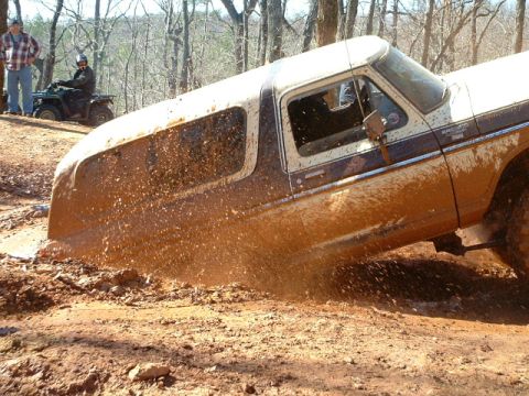 1992 Ford Mustang - A Ford Bronco is stuck in the mud during an off-road excursion, with two onlookers and an ATV nearby.