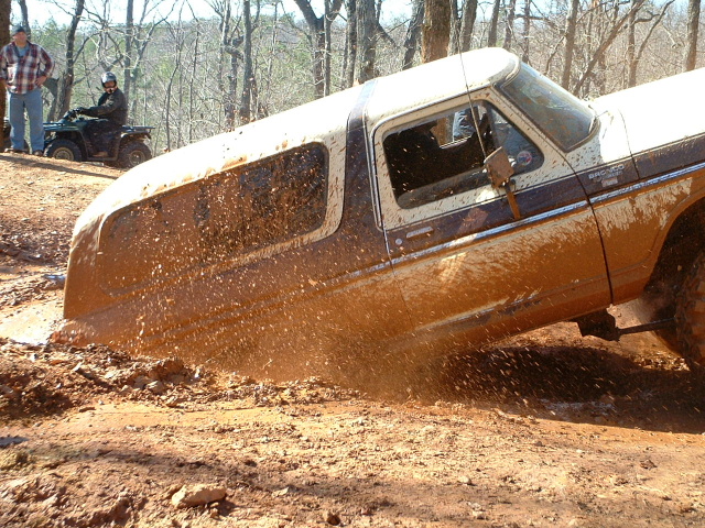 1978 Ford Bronco stuck in mud with two people and an ATV visible in the background