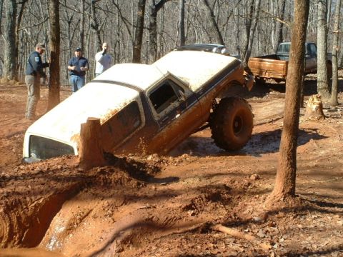 1992 Ford Mustang - A lifted truck is stuck in a deep mud pit while onlookers observe the situation.