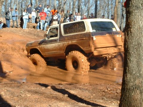 1992 Ford Mustang - A muddy off-road vehicle navigates a challenging course with spectators watching.