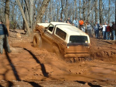 1992 Ford Mustang - An off-road SUV navigates a muddy trail with spectators watching.