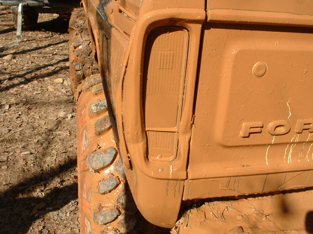 mud-covered truck rear quarter panel with taillight and 'FOR' emblem visible, next to a large off-road tire