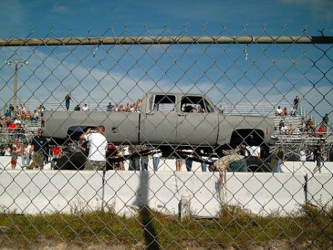 1986 Ford Bronco - A lifted pickup truck is on display with a crowd watching from bleachers in the background.