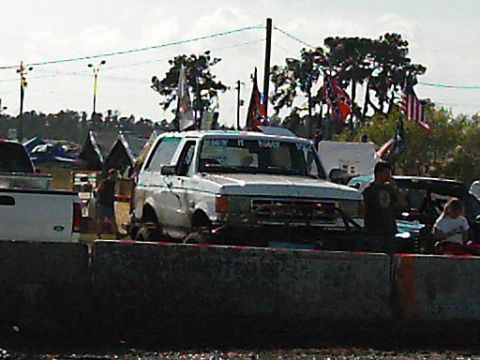 1986 Ford Bronco - A white 1986 Ford Bronco is seen with various flags displayed, participating in an event.