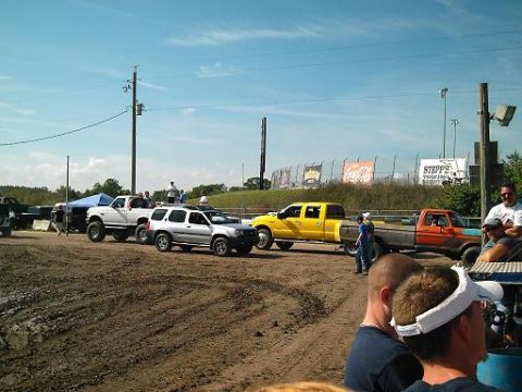 1986 Ford Bronco - Off-road vehicles are gathered at a dirt track event, with spectators watching from the side.