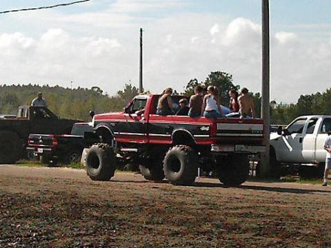 1986 Ford Bronco - This lifted Ford F-Series truck, likely from the mid-1980s, carries passengers in its bed during an outdoor event.