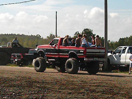 Side view of a lifted red and black Ford F-Series truck with people in the bed