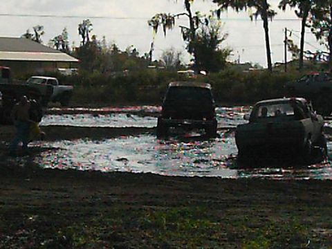1986 Ford Bronco - Multiple vehicles are stuck in a mud bog under a cloudy sky.