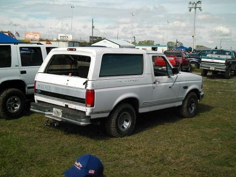 1986 Ford Bronco - White 1987 Ford Bronco with 'PATROL' text visible on the side, parked in a grassy lot with other vehicles.