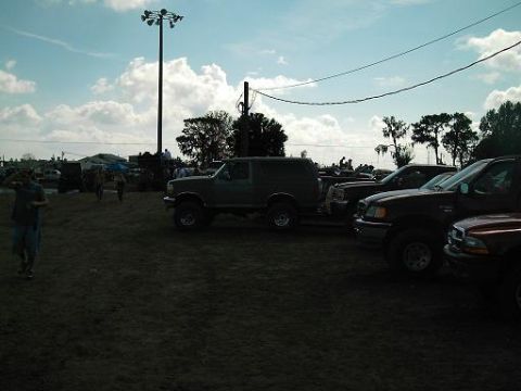1986 Ford Bronco - Several trucks and a lifted SUV are parked in an outdoor lot under a cloudy sky.