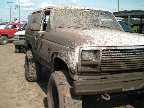 1986 Ford Bronco - This heavily mud-splattered 1986 Ford Bronco is seen from a 3q-front angle, with other vehicles visible in the background.