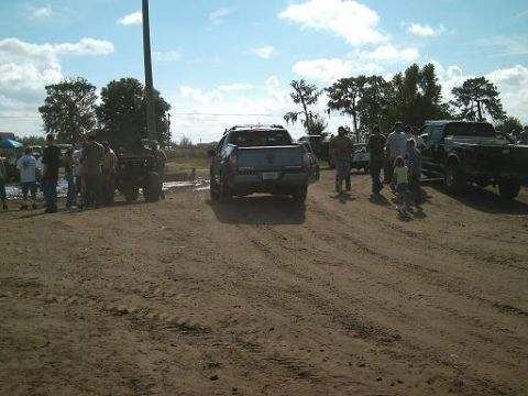 1986 Ford Bronco - Multiple trucks and people are gathered in a dirt lot on a sunny day.