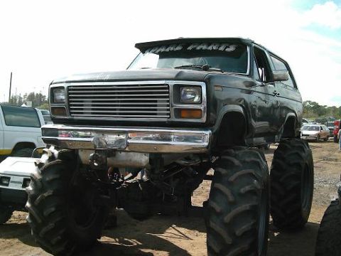 1986 Ford Bronco - Modified monster truck with oversized tires and a prominent grille, parked outdoors.