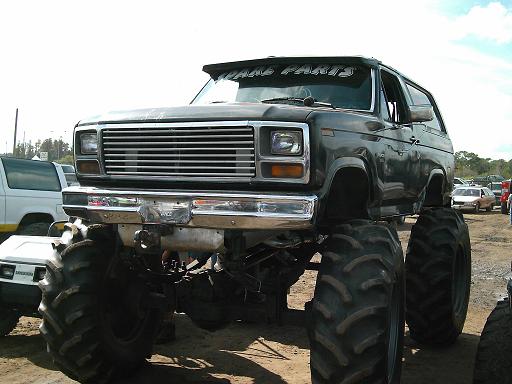 Lifted gray Ford Bronco on huge agricultural tires, front three-quarter view on a sandy lot