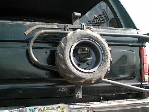 1986 Ford Bronco - A spare tire is mounted on the rear of a dark-colored SUV, attached to a custom metal carrier.