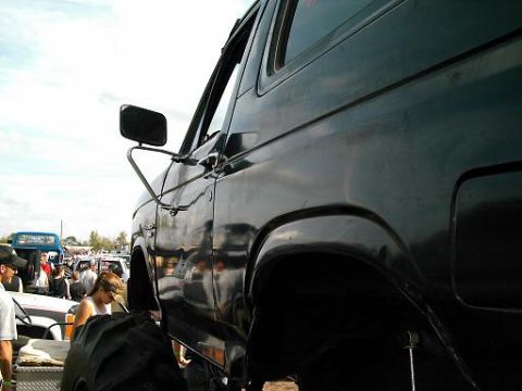 1986 Ford Bronco - A dark SUV with oversized tires is parked at an outdoor event with spectators.