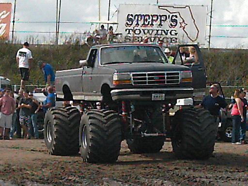 Monster truck with oversized tires and lifted suspension, front view. Grille indicates Ford F-Series