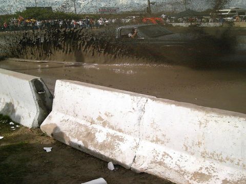 1986 Ford Bronco - A truck navigates a muddy obstacle course, sending up a large spray of water and mud.