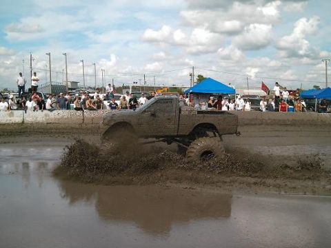 1986 Ford Bronco - A modified truck churns mud during a competition with spectators watching.