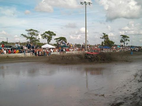 1986 Ford Bronco - Mud bog event with a red truck creating a large splash as it drives through the mire.