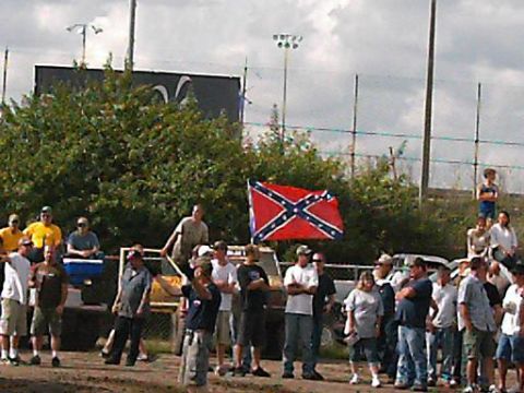 1986 Ford Bronco - A group of people are standing around a field with a large Confederate flag displayed.