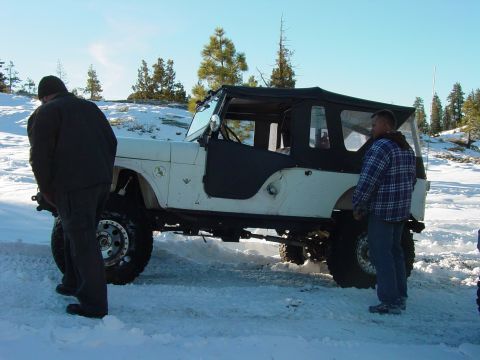 1986 Ford Bronco - A white Jeep CJ-7 with a black soft top is parked in the snow with two people standing nearby.