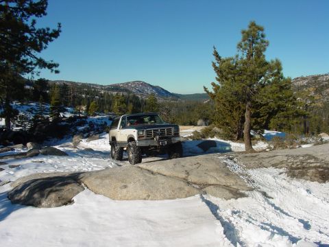 1986 Ford Bronco - A modified Ford Bronco navigates a snowy, rocky landscape under a clear blue sky.