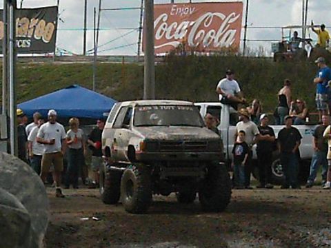 1986 Ford Bronco - A lifted 1986 Ford Bronco, covered in mud, participates in an event with spectators gathered around.