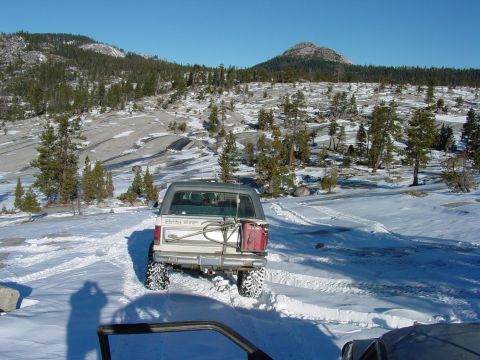 1986 Ford Bronco - A white Ford Bronco navigates a snowy, mountainous terrain with tire tracks visible in the snow.