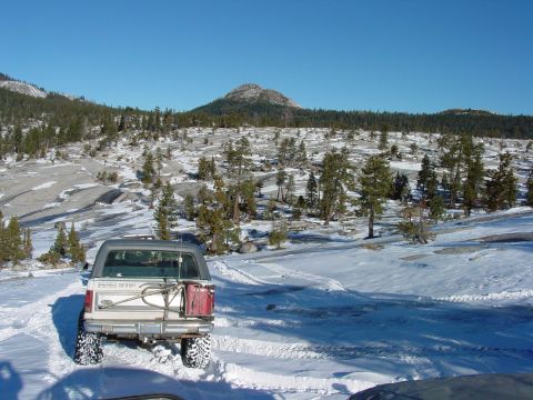 1986 Ford Bronco - A white 1986 Ford Bronco navigates a snowy terrain, equipped with a spare tire carrier and a red jerry can.