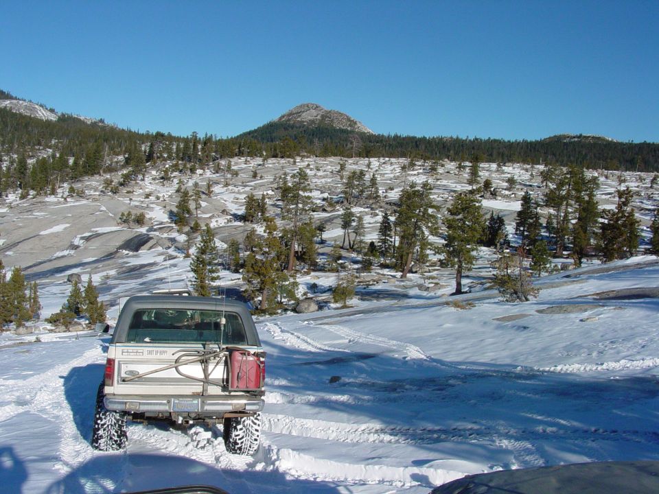 Rear view of a white 1986 Ford Bronco in a snowy landscape with a red jerry can on the spare tire carrier