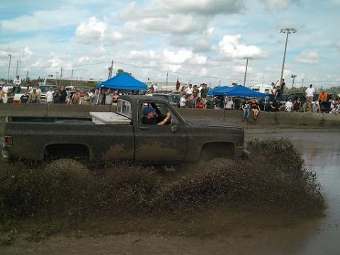 1986 Ford Bronco - A truck churns up mud during an event, with a crowd watching from the sidelines.