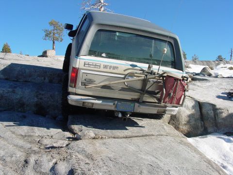 1986 Ford Bronco - 1986 Ford Bronco navigates rocky terrain, displaying a bike rack and a humorous bumper sticker.