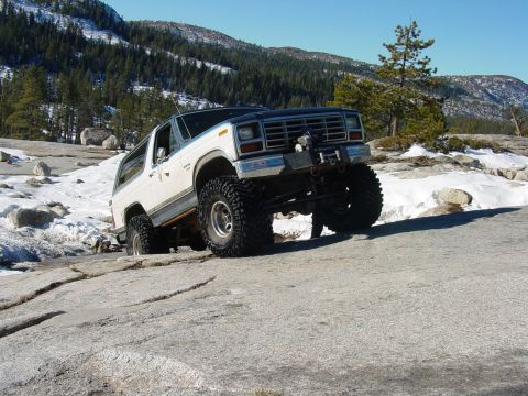 1986 Ford Bronco - This modified Ford Bronco navigates a challenging rocky terrain with snow patches visible.