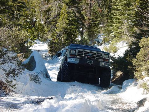 1986 Ford Bronco - A dark colored Ford Bronco navigates a snow-covered trail through a forest.