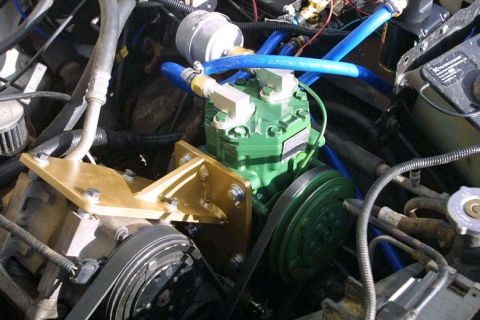 1993 Ford Bronco - Engine-bay close-up of an engine-driven onboard air compressor setup: a green-painted York-style compressor on a gold powder-coated bracket…