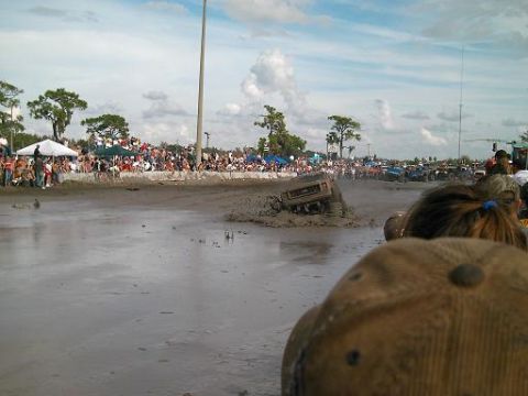 1986 Ford Bronco - A truck is stuck in the mud during a mud bogging event, with a large crowd of spectators in the background.