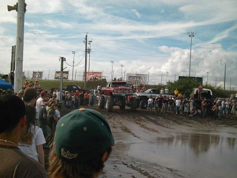 1986 Ford Bronco - A mud bogging event features monster trucks navigating a muddy track as a crowd of spectators observes.
