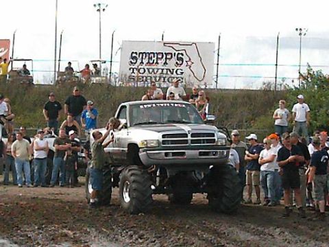 1986 Ford Bronco - A lifted Dodge pickup truck with large tires is the center of attention at an outdoor event.