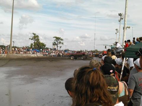 1986 Ford Bronco - A muddy track hosts a monster truck event with a large crowd watching from the sidelines.