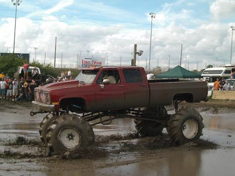 1986 Ford Bronco - A heavily modified red pickup truck navigates a muddy track, likely at a motorsports event.