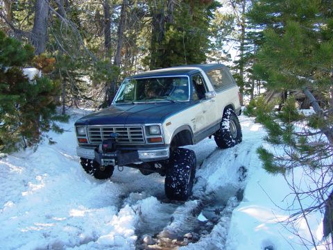 1986 Ford Bronco - Modified Ford Bronco navigates a snow-covered path in a wooded area.