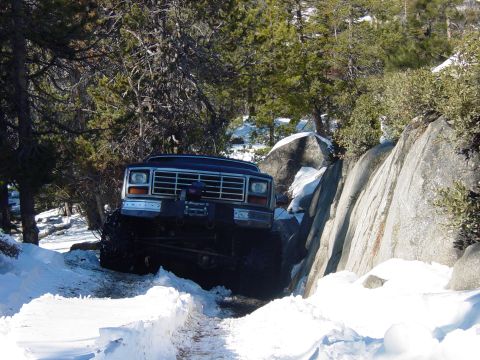 1986 Ford Bronco - A modified Ford Bronco navigates a challenging off-road path covered in snow and rocks.