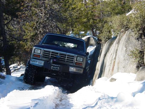 1986 Ford Bronco - A dark blue Ford Bronco navigates a snowy, rocky trail.