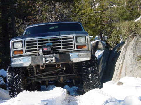 1986 Ford Bronco - A dark blue 1986 Ford Bronco equipped with a winch tackles a challenging snowy and rocky trail.