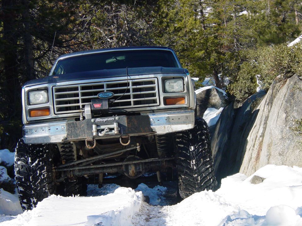 Dark blue 1986 Ford Bronco with winch on front bumper navigating rocky, snowy terrain