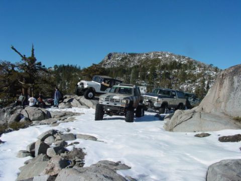 1986 Ford Bronco - Several off-road vehicles are parked on a rocky, snow-covered terrain with a mountainous backdrop.
