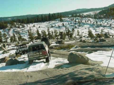 1986 Ford Bronco - Off-road vehicles navigate a challenging snowy and rocky landscape with scattered pine trees.