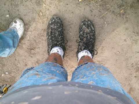 1986 Ford Bronco - Two pairs of feet, one in white sneakers and the other in black sneakers, are covered in mud.